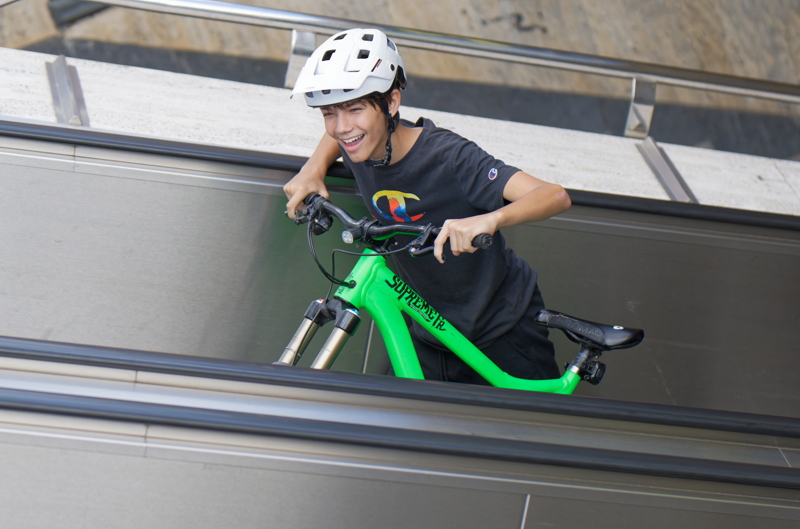 25 - Person confidently navigating a neon green Commencal Supreme FR mountain bike with a distinctive black graphic on the frame on an escalator